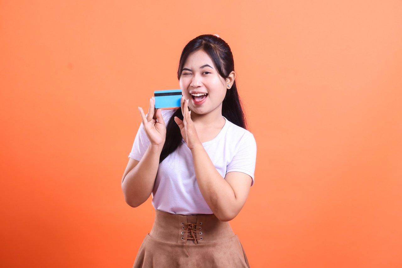 Jeune femme joyeuse tenant une carte de crédit bleue, exprimant la fidélité client.